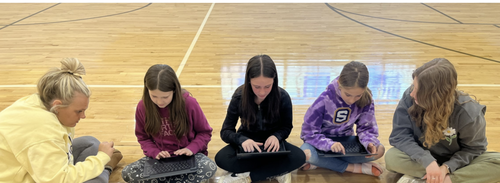 Five girls work on laptops in gymnasium